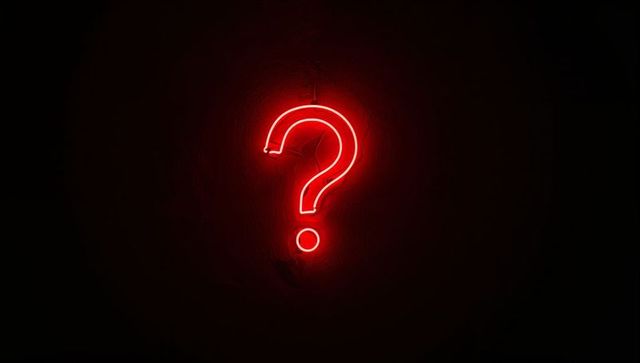 Crimson Neon Question Mark Emitting Halo and Illuminated Dot on Dark Textured Wall