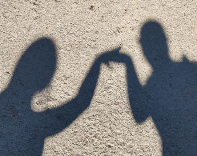 Two shadows outline on sandy ground, extending hands and touching fingers. Ideal for concepts of friendship, connection, and human interaction in creative projects, photography portfolios, and social media content.