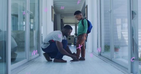 Father kneeling tying son's shoelaces in bright modern hallway preparing for school
