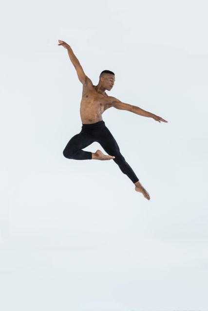 Male ballet dancer leaping gracefully in a studio. Ideal for use in articles or advertisements related to dance, fitness, athleticism, and the arts. Perfect for promoting dance classes, performances, and fitness programs.