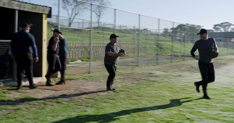 Diverse baseball teammates practicing by dugout, senior player holding glove and phone