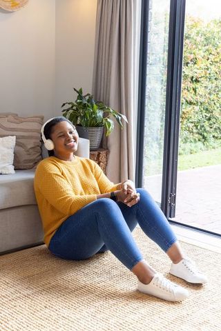 Relaxing african american woman listening to music with headphones by sliding glass door