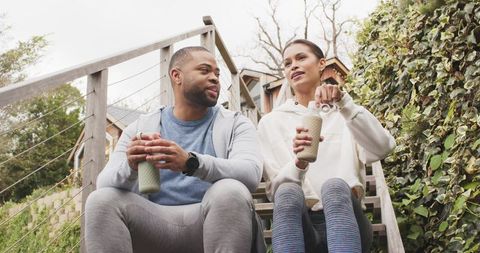 Couple relaxing after workout on outdoor stairs holding reusable bottles