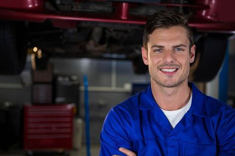 Male Mechanic Standing Under Hydraulic Lift Wearing Blue Coveralls