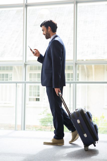 Businessman with trolley bag using mobile phone at conference centre