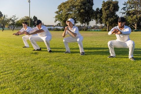 Four male athletes performing synchronized squats during outdoor warmup on sunlit field