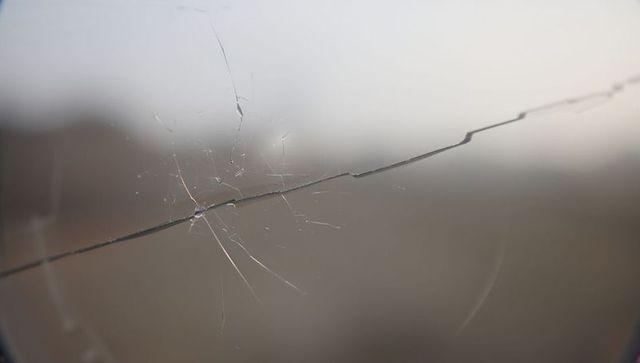 Horizontal windshield crack close-up with central impact and spiderweb fracture pattern