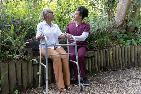 Caregiver supporting senior african american woman holding hands with walker in garden