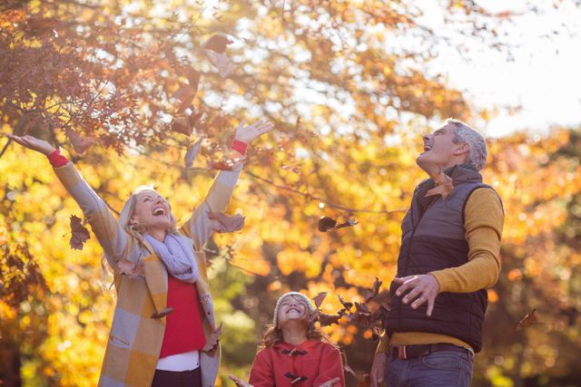 Family enjoying a playful moment in an autumn park, throwing leaves in the air. Ideal for use in advertisements, family-oriented content, seasonal promotions, and lifestyle blogs.