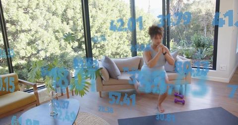 Woman doing single-leg squat at home with smartwatch, shorts, sunlit living room plants