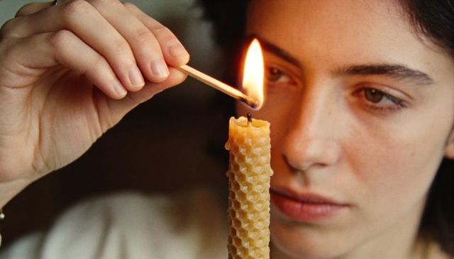 Woman lighting beeswax candle with match closeup warm flame intimate glow