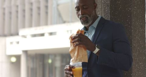 Senior african-american professional eating sandwich drinking orange juice urban lunch break