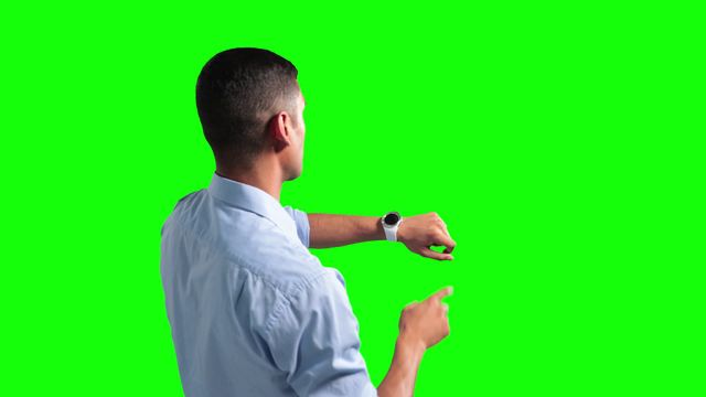 Young businessman interacts with his smartwatch. Perfect for business tech, futuristic concepts. Green screen backdrop facilitates isolation for creative projects, technology advertisements, promotional content for wearable tech. Emphasis on using new technology efficiently in a business environment. Great for illustrating time management and business productivity.