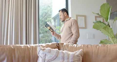 Mature man reading book by sunlit home window