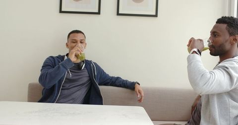 Two friends drinking green smoothies on bench wearing hoodies casual cafe conversation