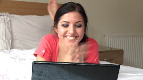 Joyful Woman Engaging with Laptop While Relaxing on Bed