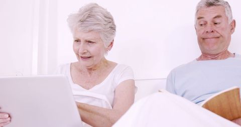 Senior Couple Relaxing at Home Reading and Using Laptop