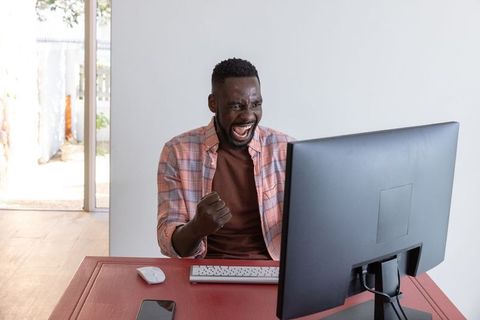 Excited man celebrating success at desk with computer