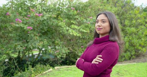 Confident woman standing in garden wearing burgundy turtleneck with arms crossed