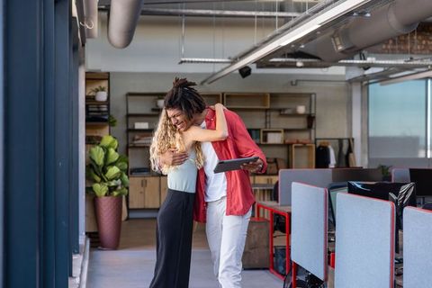 Diverse Coworkers Embracing in Modern Open-Plan Office