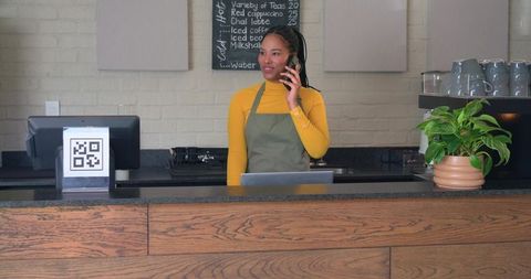 African american barista talking on phone behind minimalist coffee counter with qr sign
