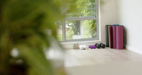 Sunlit home yoga corner with purple mats dumbbells rolled towels on pale wood floor