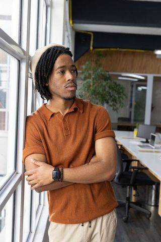 African american man leaning by window and gazing thoughtfully in modern coworking office