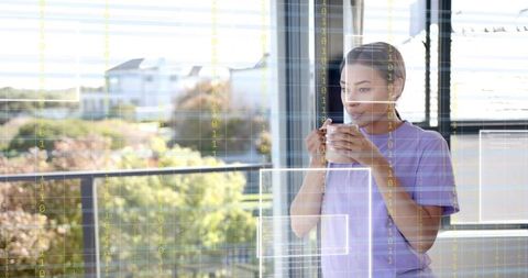 Woman sipping coffee on balcony while gazing through binary data overlay, tech wellness