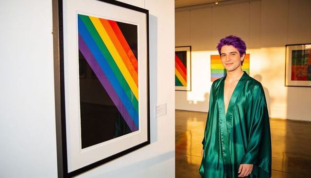 Young man with purple hair wearing green satin robe viewing rainbow artwork in gallery