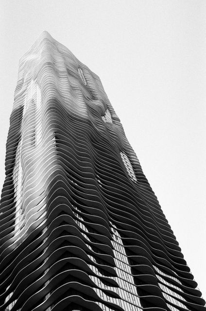Features a striking skyscraper with an innovative wave-like facade captured in black and white. Ideal for use in architectural magazines, city planning presentations, modern art galleries, and minimalist design blogs, providing a contemporary urban aesthetic.