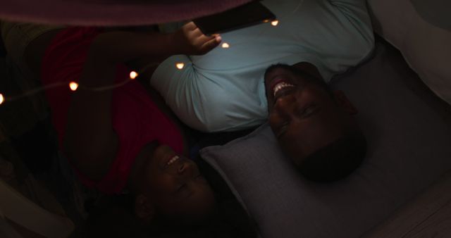 Father and daughter enjoying reading together under a blanket fort decorated with fairy lights. Perfect for concepts of family bonding, bedtime routines, childhood memories, parenting moments, and indoor activities.