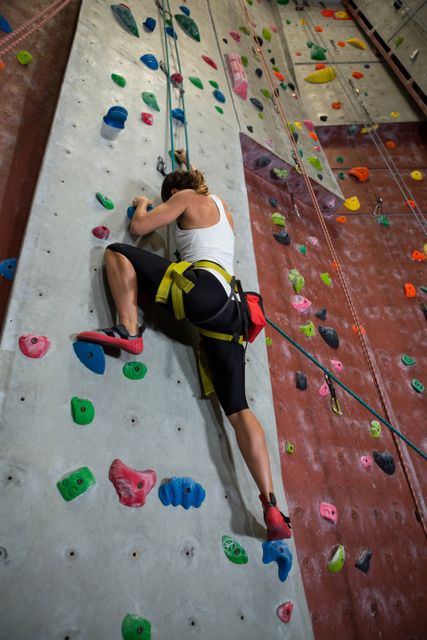 Woman climbing indoor rock wall, showcasing determination and athleticism. Ideal for use in fitness, sports, and adventure-related content. Perfect for promoting active lifestyles, gym memberships, and climbing gear.