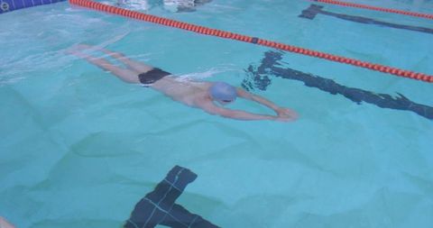 Male swimmer gliding in lap lane with blue cap and black trunks, minimal aerial pool view