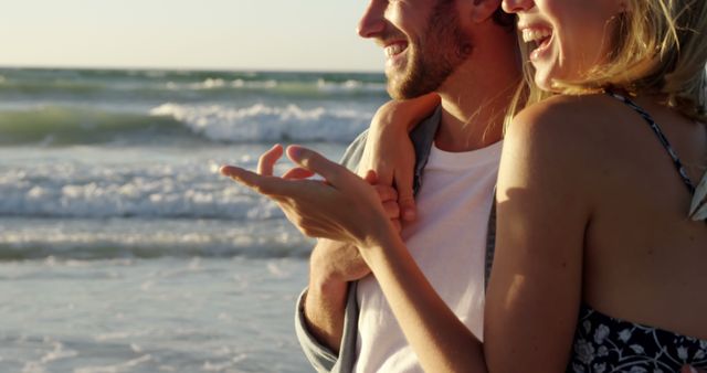 A young Caucasian couple enjoys a romantic moment on the beach at sunset, with copy space. Their shared laughter and closeness capture a carefree and intimate connection against the backdrop of the ocean.