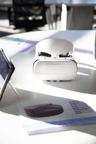White vr headset resting on meeting table, tablet and printed business charts in sunlight