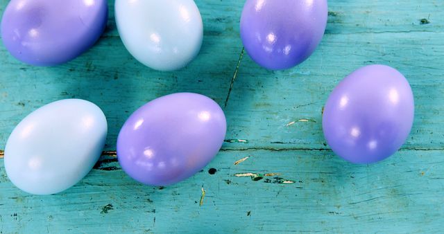 Purple and white Easter eggs are scattered on a rustic blue wooden surface, with copy space. Their pastel colors suggest a festive springtime theme, often associated with Easter celebrations.