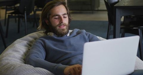 Casual work environment: man relaxing on beanbag with laptop in office