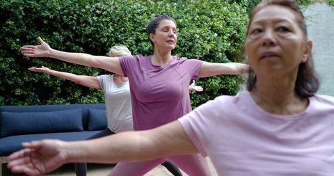 Multigenerational women practicing yoga on backyard patio with hedge and blue sofa