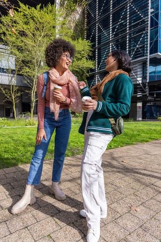 African american and asian students laughing while holding coffee on campus courtyard