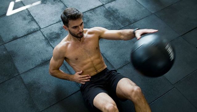Shirtless man twisting with medicine ball on gym floor building core strength and rotation
