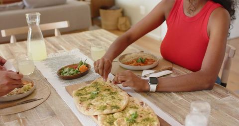 Woman tearing herb flatbread sharing casual rustic dinner with smartwatch on wrist