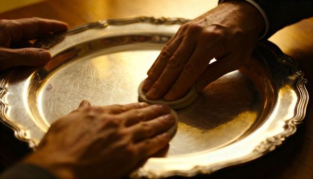 Polishing silver serving tray with hands buffing patina on warm wooden tabletop