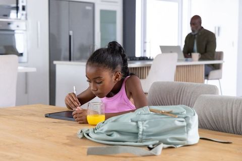 African american girl drawing on tablet at table while father working on laptop