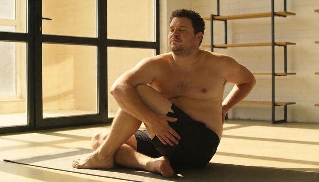 Plus-size man practicing seated twist yoga in sunlit minimalist studio for mindful stretching
