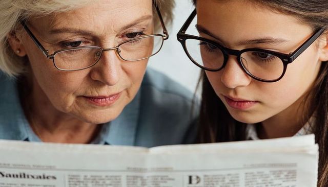 Grandmother and granddaughter reading newspaper together closeup sharing moment