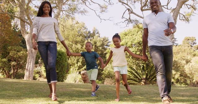 Depicts an African American family of four enjoying a walk in a sunny park. Useful for concepts related to family bonding, outdoor activities, healthy living, and happy moments.
