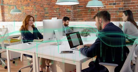 Business team collaborating in modern open-plan office with exposed brick and laptops