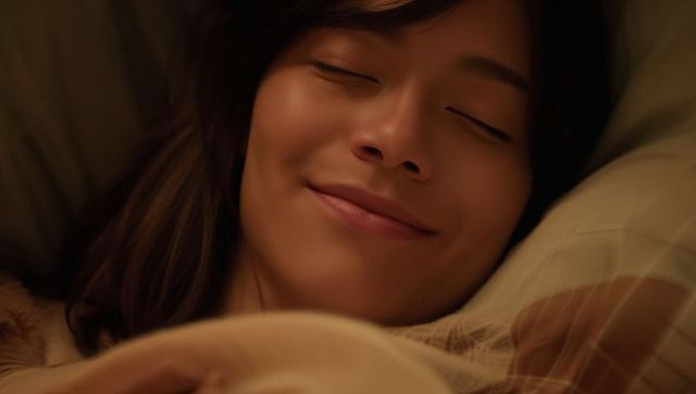 Smiling woman resting peacefully in bed wearing sleepwear with striped pillow and duvet