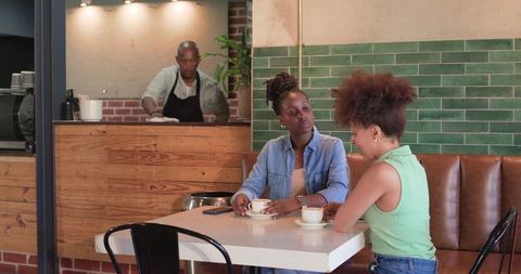 African American women chatting over coffee in cozy cafe while barista wiping counter