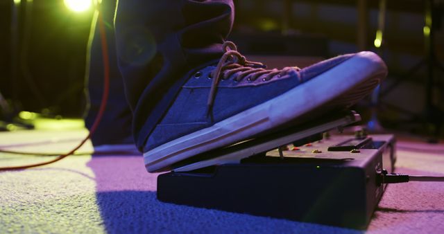 Musician's foot pressing guitar effects pedal during a live performance. Highlights the interaction between musician and instrument. Ideal for content related to live music events, musical equipment, performances, bands, and musical instruction.